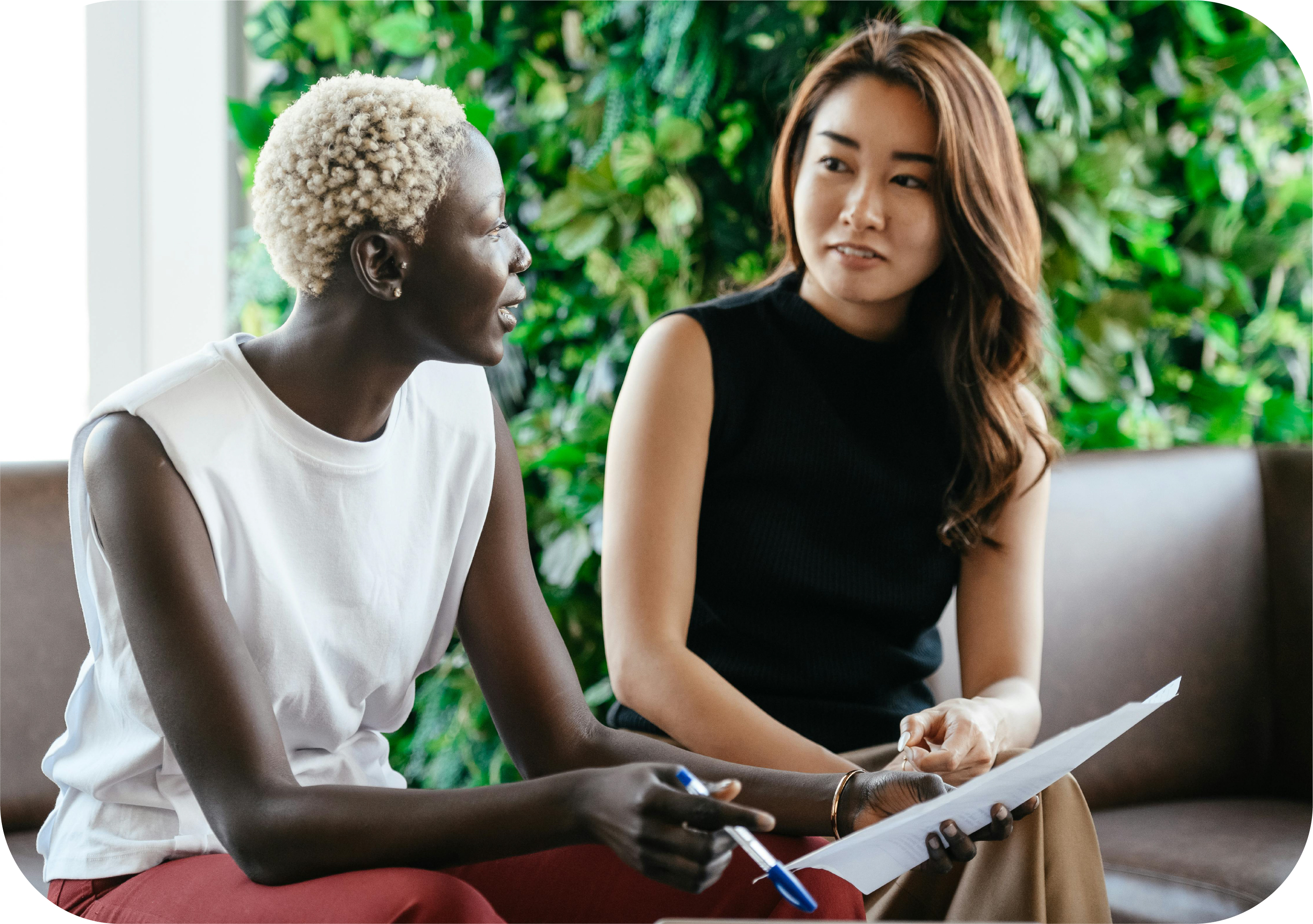 An image of two women sitting and discussing something; the woman on the left is holding a pen and paper as she explains something.