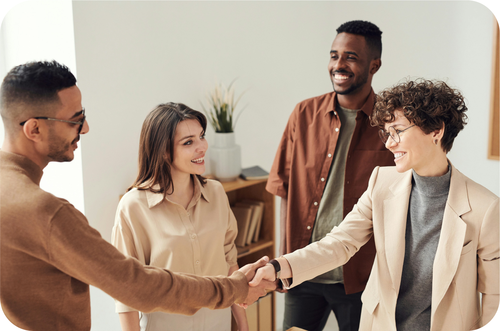 A group of four people all smiling; the two in the front are shaking hands in agreement.